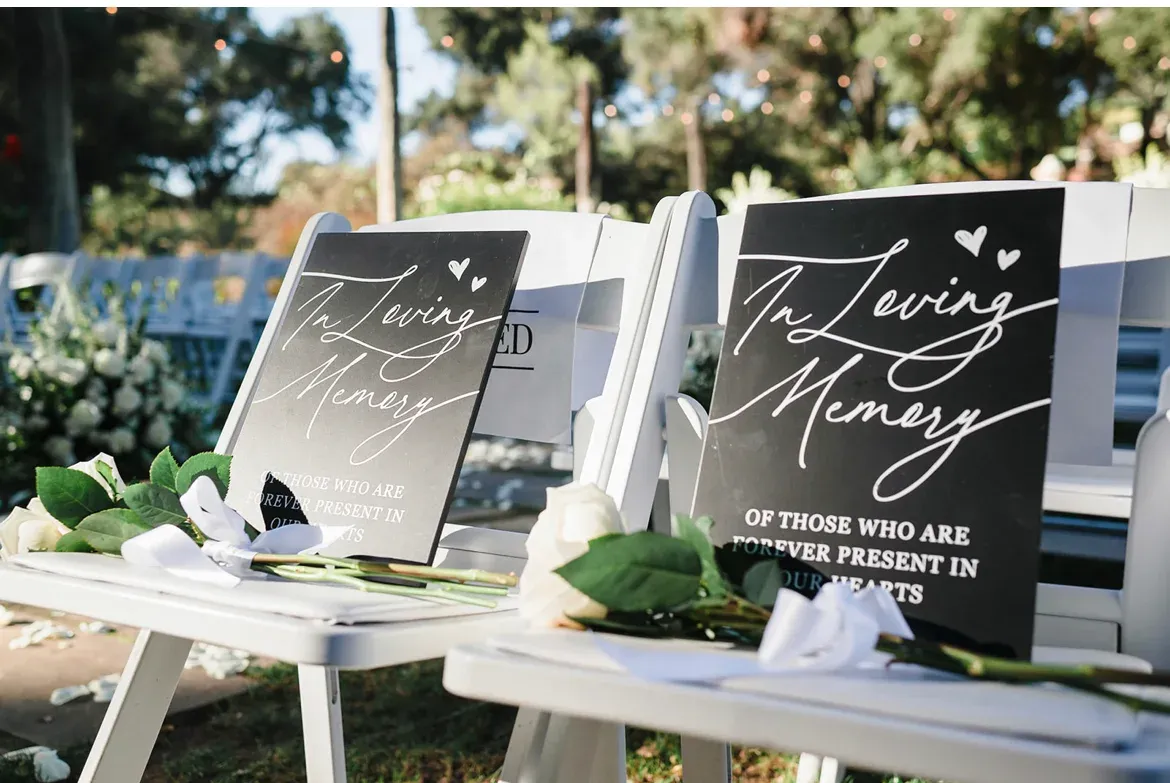 A small hand-lettered remembrance sign honoring loved ones no longer present, dressed with white roses.