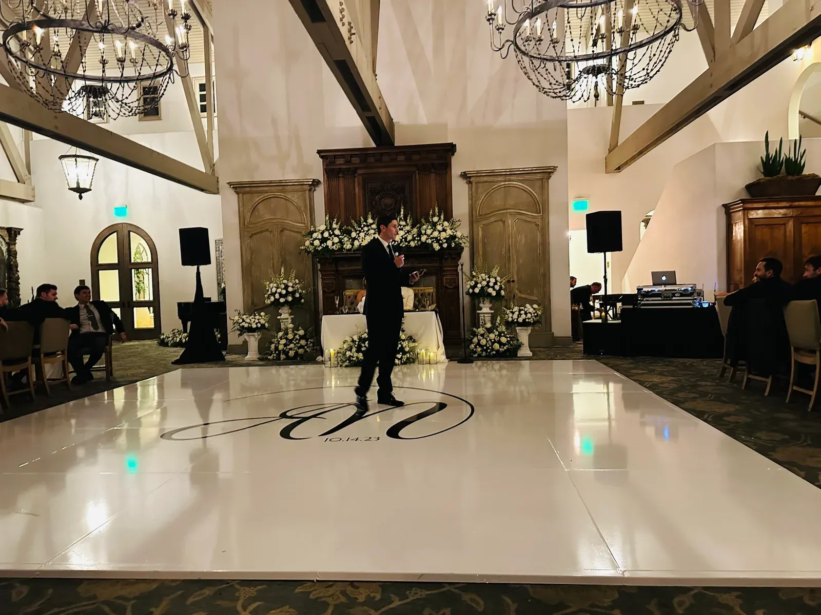 A pale monogrammed dance floor at the center of the historic estate room, ringed by candlelit tables.