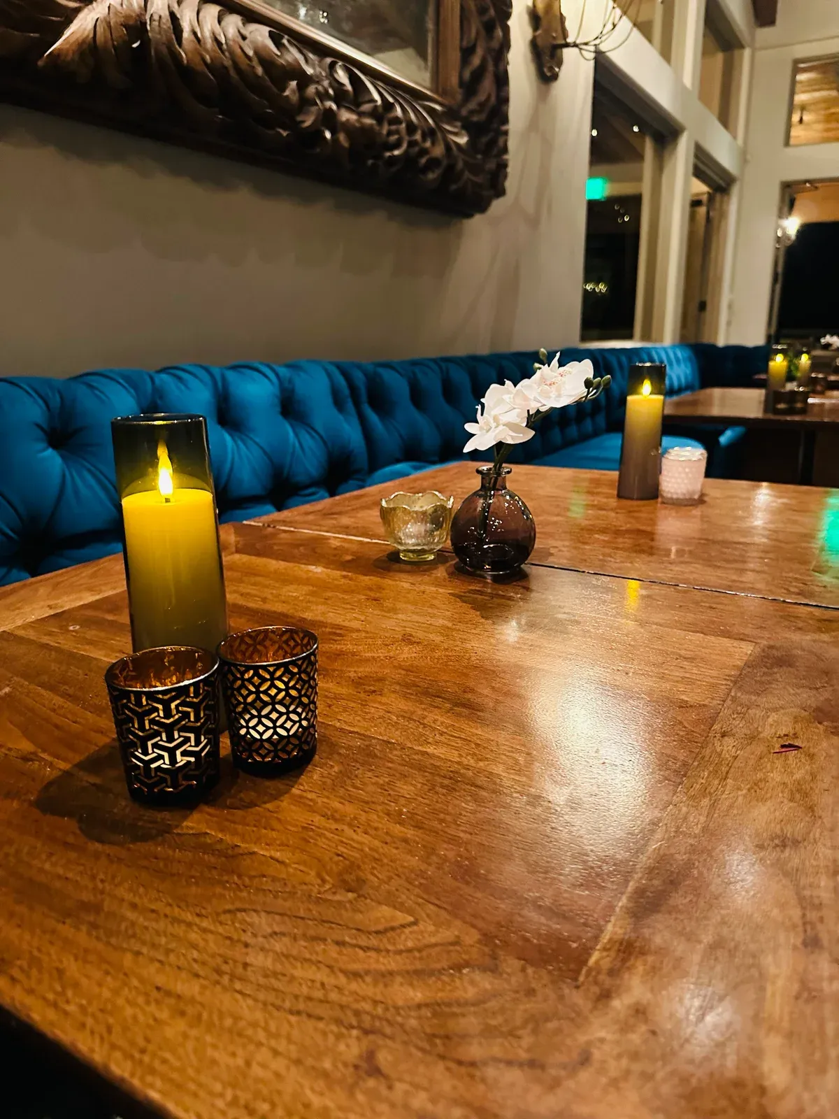 Deep teal velvet seating beside a long candlelit table in a walnut-paneled estate room.